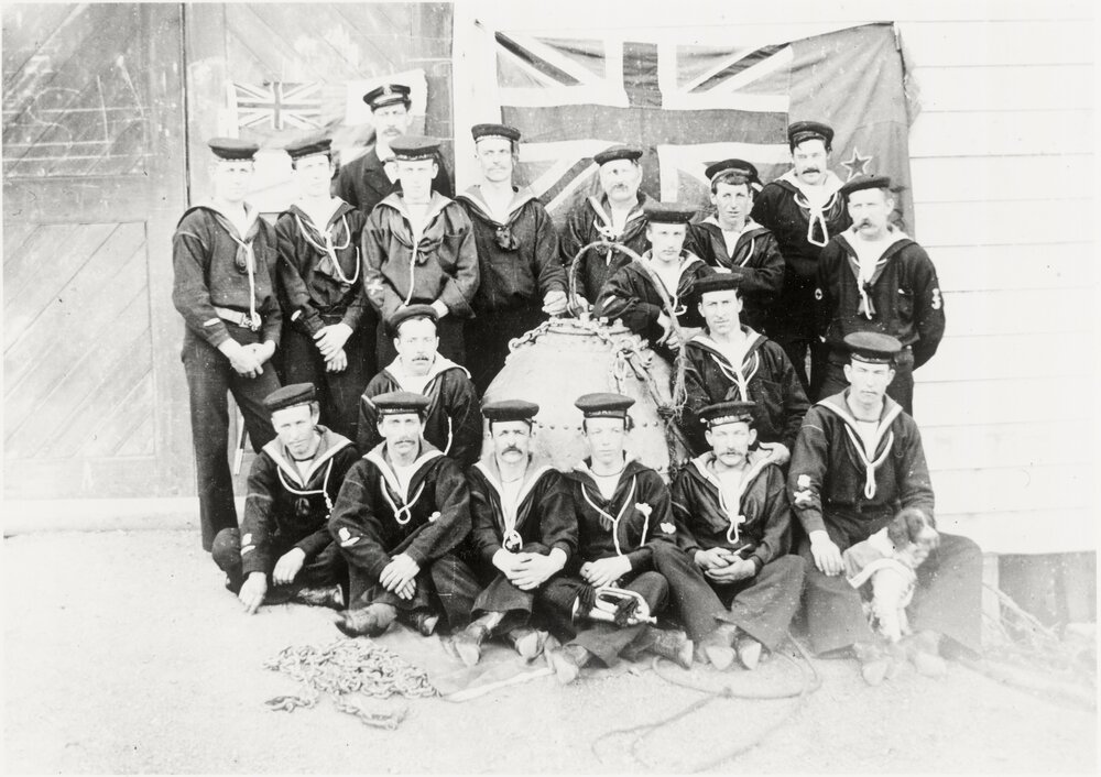 Group of Petone navals with flags on the wall behind